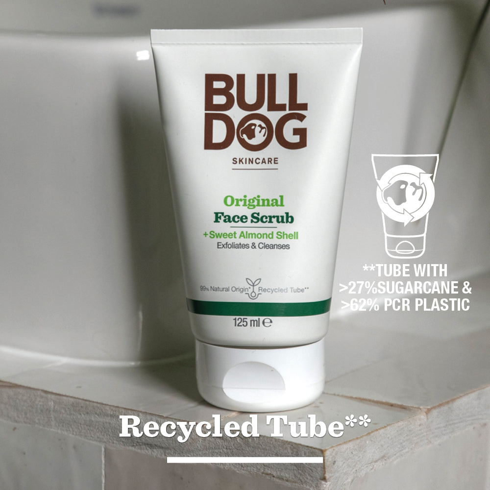 A tube of Original Face Scrub stands on a bathroom surface, featuring a recycled tube made with 27% sugarcane, 62% PCR plastic, and natural origin ingredients like sweet almond shell.