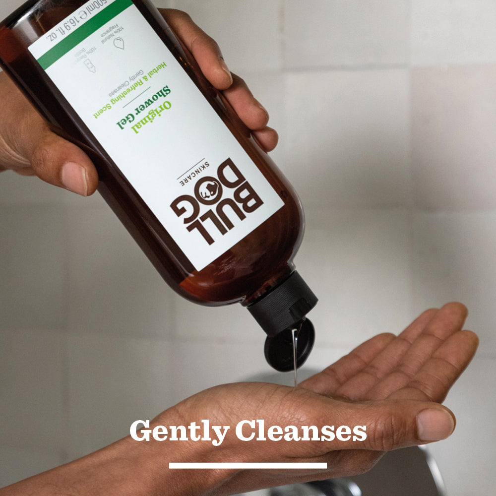 A person sprays Bull Dog Original Spray Deodorant Bundle onto their underarm over a sink. The text Gently Protects appears at the bottom of the image.