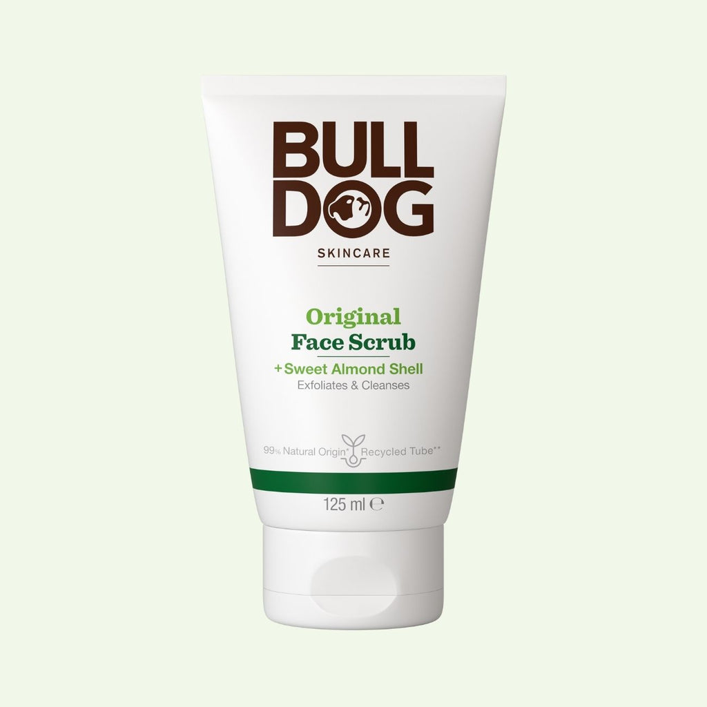 A white 125 ml tube of Original Face Scrub for men, made with sweet almond shell and natural origin ingredients, stands upright against a pale background. The front displays green and brown text.